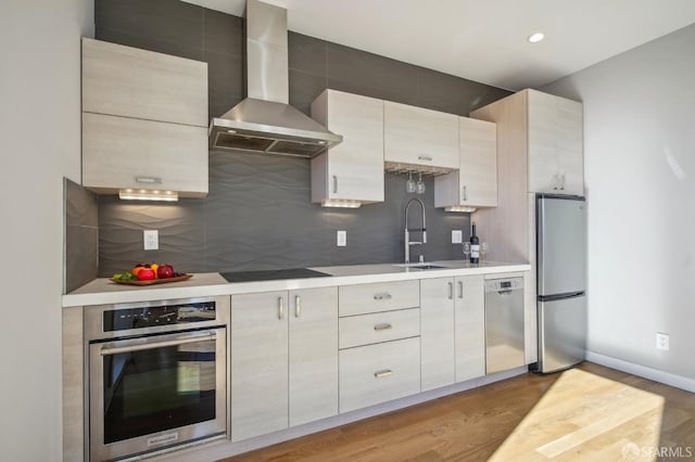 kitchen featuring wall chimney exhaust hood, sink, tasteful backsplash, stainless steel appliances, and light hardwood / wood-style floors