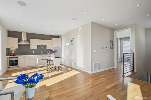 kitchen with appliances with stainless steel finishes, sink, decorative backsplash, light hardwood / wood-style floors, and wall chimney range hood