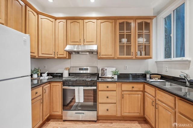 kitchen featuring dark stone counters, stainless steel gas range, sink, and white fridge