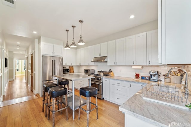 kitchen featuring white cabinetry, premium appliances, pendant lighting, and a breakfast bar area