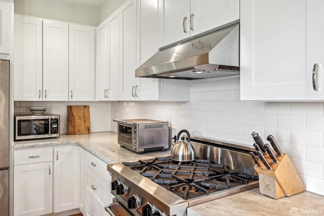 kitchen with light stone countertops, white cabinets, stainless steel appliances, and tasteful backsplash