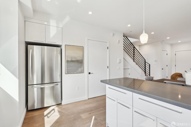 kitchen with hanging light fixtures, light hardwood / wood-style floors, stainless steel refrigerator, and white cabinets