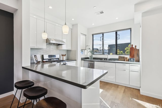 kitchen featuring a kitchen bar, kitchen peninsula, white cabinets, and appliances with stainless steel finishes