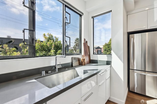 kitchen featuring dark wood-type flooring, sink, white cabinetry, dark stone countertops, and stainless steel refrigerator