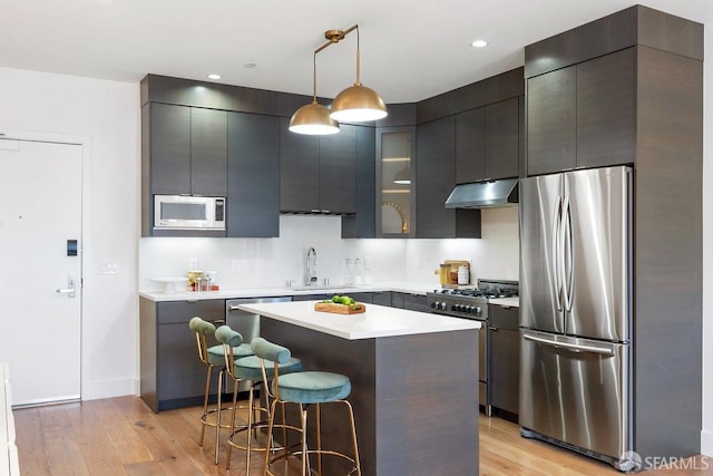 kitchen featuring appliances with stainless steel finishes, light wood-type flooring, a kitchen island, and hanging light fixtures