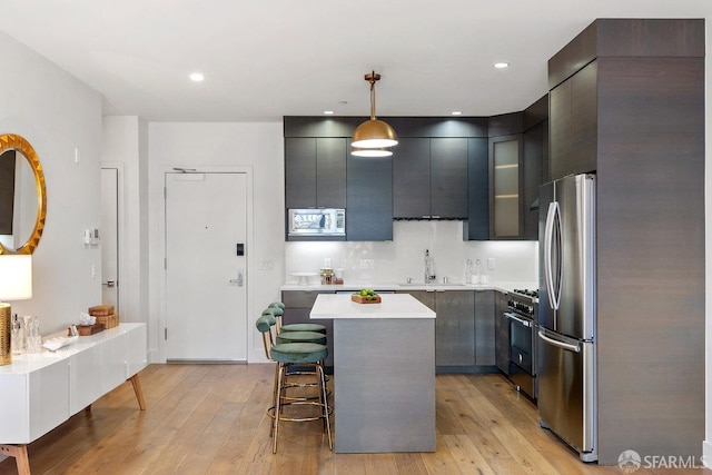 kitchen with a kitchen island, light hardwood / wood-style floors, stainless steel appliances, decorative light fixtures, and a breakfast bar