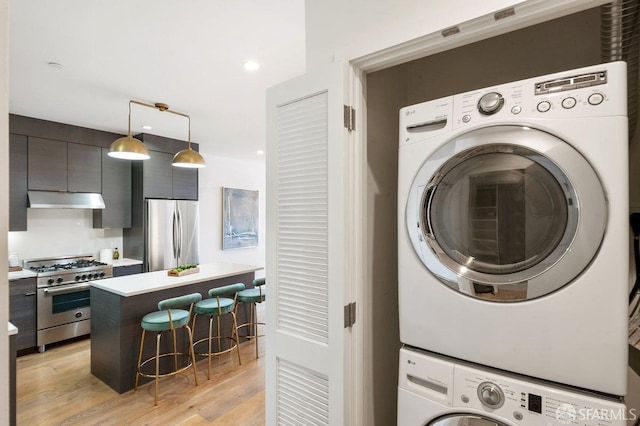 laundry room with stacked washer / drying machine and light wood-type flooring