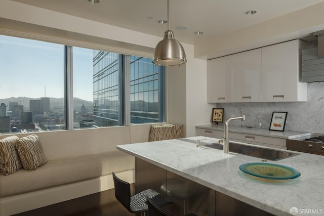 kitchen with sink, hanging light fixtures, light stone countertops, white cabinets, and decorative backsplash