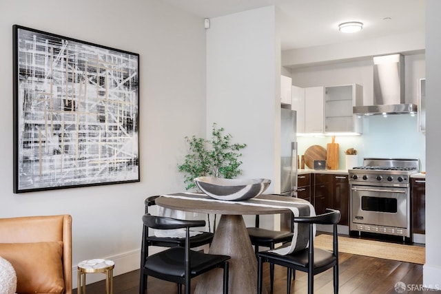 kitchen featuring wall chimney range hood, appliances with stainless steel finishes, dark wood finished floors, and light countertops