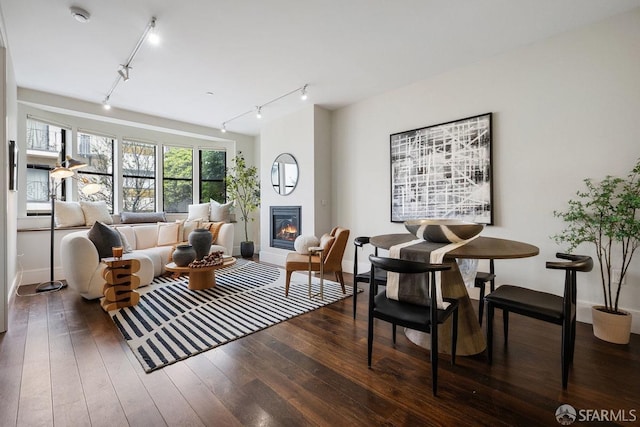 living room featuring hardwood / wood-style flooring, rail lighting, baseboards, and a glass covered fireplace