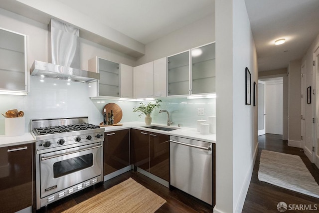 kitchen featuring light countertops, appliances with stainless steel finishes, glass insert cabinets, a sink, and wall chimney range hood