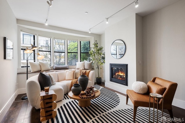 sitting room featuring dark wood-style floors, track lighting, a glass covered fireplace, and baseboards