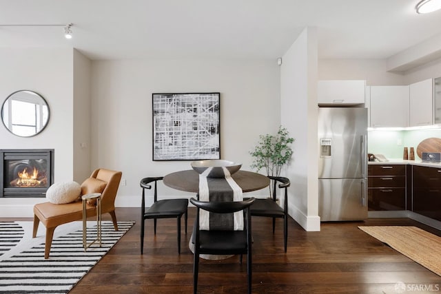 dining area featuring dark wood-style floors, a glass covered fireplace, and baseboards