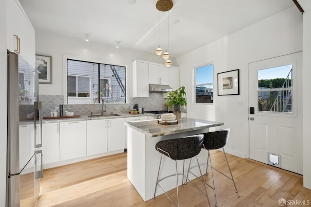 kitchen featuring stainless steel appliances, sink, a center island, white cabinetry, and hanging light fixtures