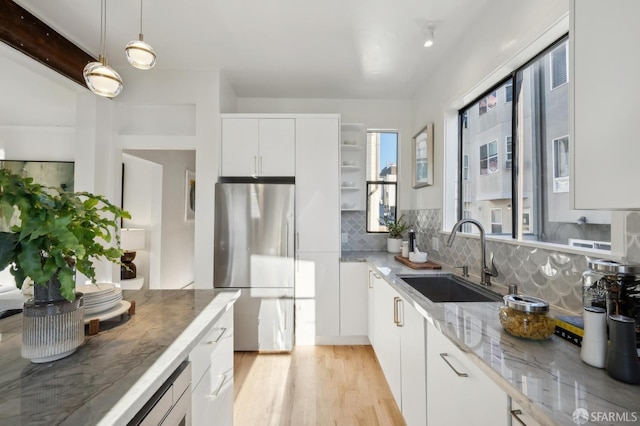 kitchen featuring stainless steel refrigerator, sink, hanging light fixtures, backsplash, and white cabinets