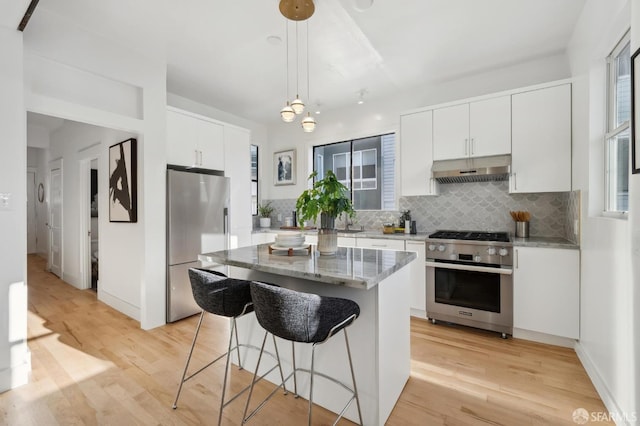 kitchen featuring white cabinets, hanging light fixtures, decorative backsplash, appliances with stainless steel finishes, and a kitchen island