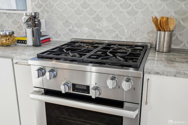 details with stainless steel gas range oven, light stone counters, and tasteful backsplash