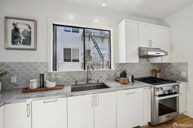 kitchen featuring light stone countertops, backsplash, high end stove, sink, and white cabinets