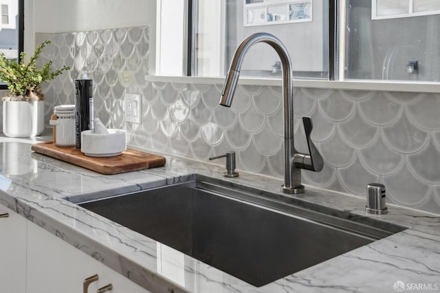 interior details featuring light stone countertops, decorative backsplash, white cabinets, and sink