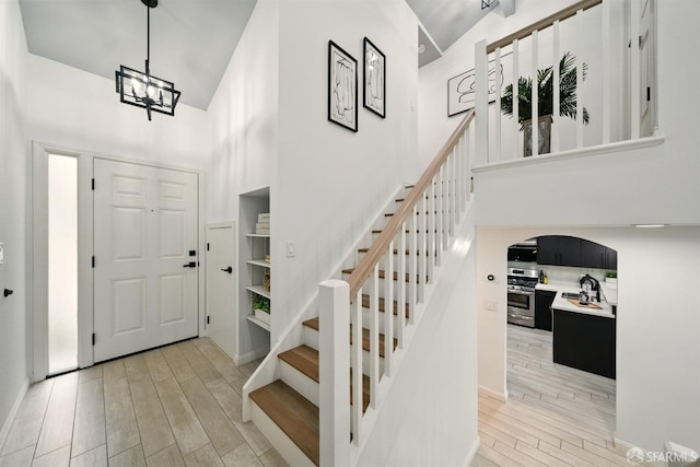 foyer entrance with arched walkways, light wood-type flooring, high vaulted ceiling, a notable chandelier, and stairs