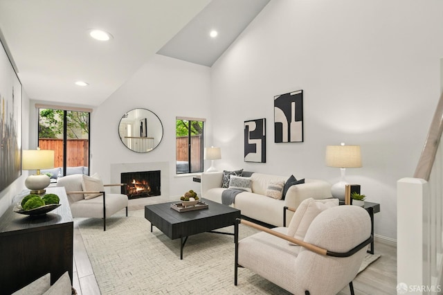 living room featuring recessed lighting, baseboards, a warm lit fireplace, and high vaulted ceiling