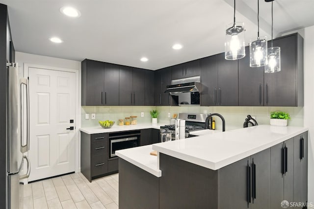 kitchen with a peninsula, under cabinet range hood, a sink, backsplash, and stainless steel appliances