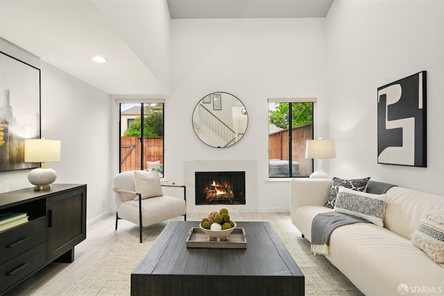 living room featuring plenty of natural light, a warm lit fireplace, light wood-style flooring, and a high ceiling