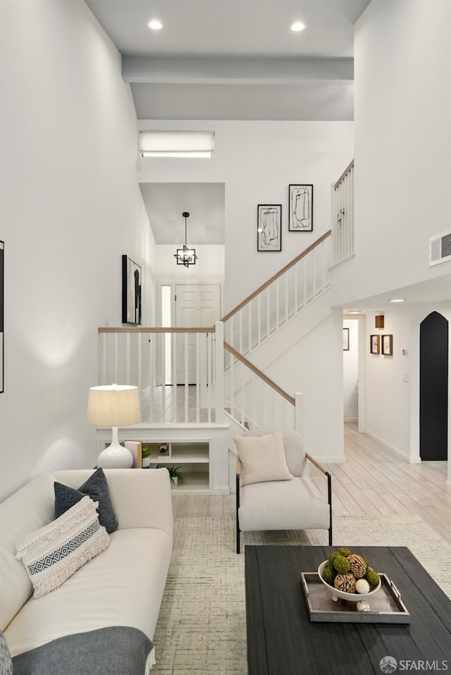living room with a high ceiling, arched walkways, a chandelier, stairs, and visible vents