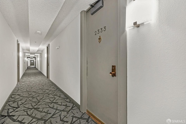 hallway with carpet flooring, a textured ceiling, and baseboards