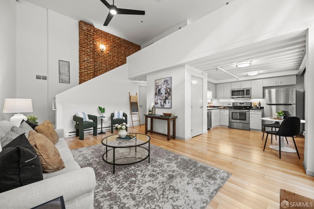 101 Harrison St Unit 102, San Francisco, CA 94105 - living room with a baseboard radiator, a ceiling fan, a towering ceiling, and light wood-style flooring