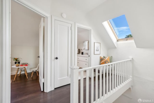 hall featuring lofted ceiling with skylight, baseboards, dark wood-style flooring, and an upstairs landing