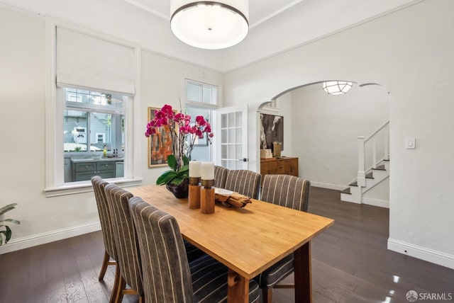 dining area with wood-type flooring, stairs, arched walkways, and baseboards