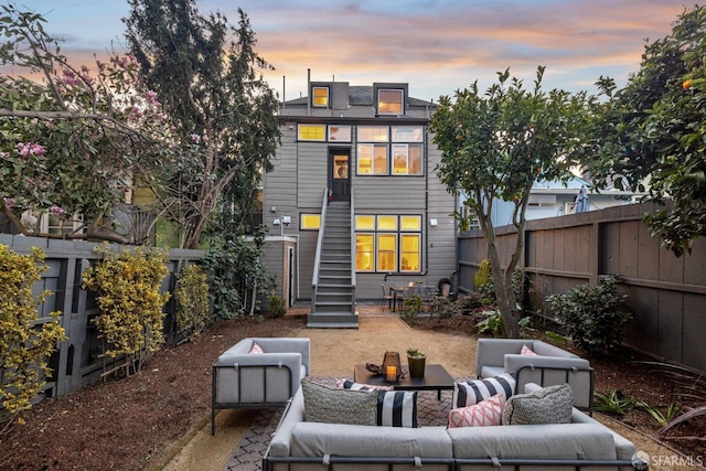 back of house at dusk with a fenced backyard, stairway, and an outdoor hangout area