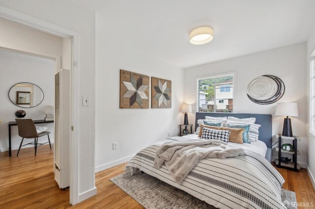 bedroom featuring baseboards, wood finished floors, and a heating unit
