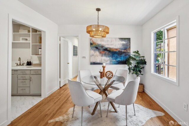 dining area featuring indoor wet bar, baseboards, a chandelier, and light wood-style floors