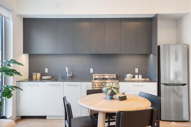 kitchen with white cabinets, stainless steel fridge, sink, and tasteful backsplash