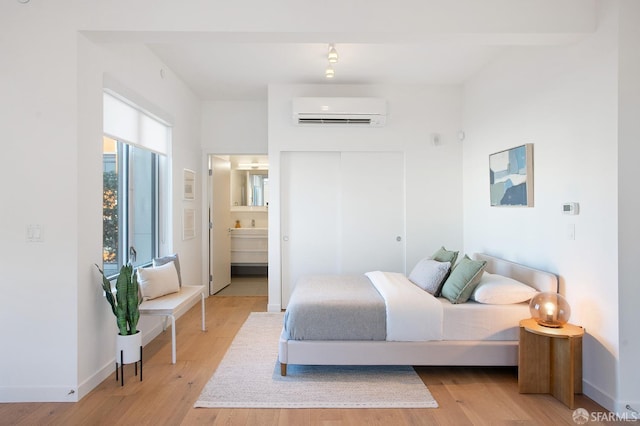 bedroom with ensuite bath, light wood-type flooring, and a wall mounted AC