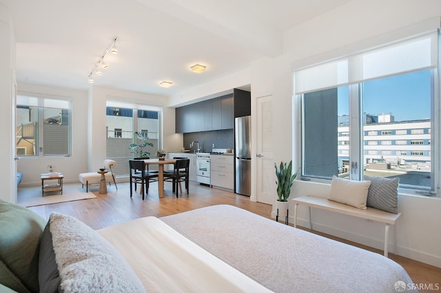 bedroom with stainless steel fridge, light hardwood / wood-style flooring, multiple windows, and beam ceiling