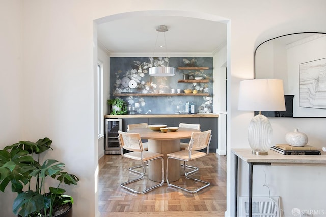 bar featuring hanging light fixtures, parquet flooring, crown molding, and wine cooler