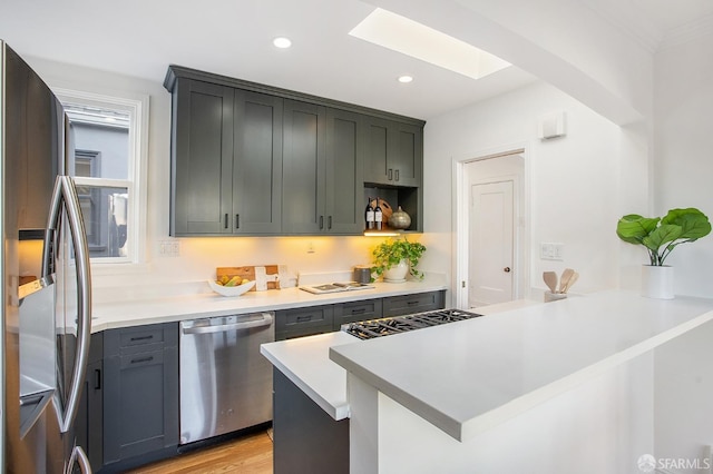 kitchen with kitchen peninsula, appliances with stainless steel finishes, a skylight, and light hardwood / wood-style flooring