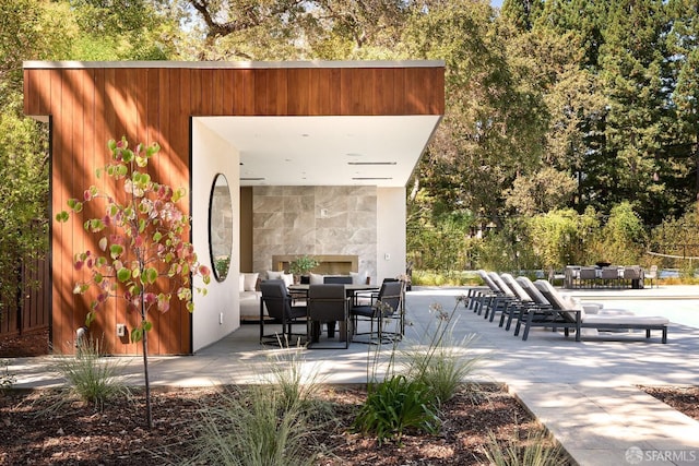 view of patio featuring exterior fireplace, outdoor dining area, and view of scattered trees