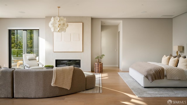 bedroom featuring wood finished floors, a glass covered fireplace, a chandelier, and baseboards