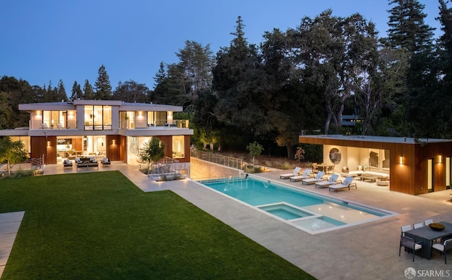 back house at dusk featuring a balcony, a pool with hot tub, a lawn, outdoor lounge area, and a patio area