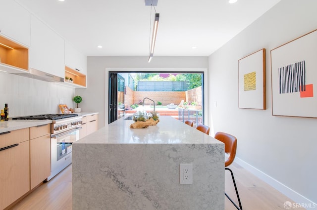 kitchen with high end stainless steel range, sink, a center island, a kitchen breakfast bar, and light hardwood / wood-style floors