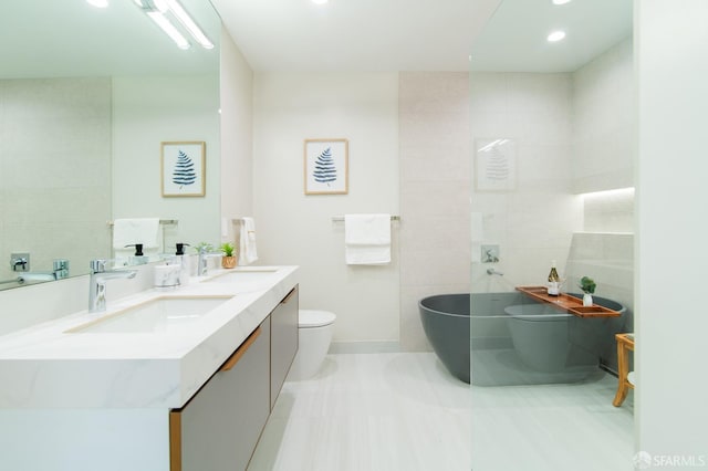 bathroom with tile walls, a tub to relax in, vanity, toilet, and tile patterned floors