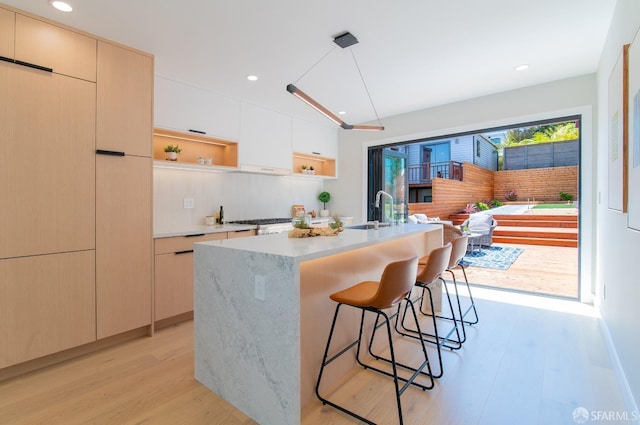 kitchen featuring sink, decorative light fixtures, a center island with sink, light wood-type flooring, and a kitchen breakfast bar