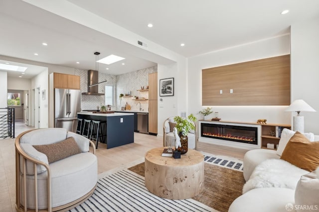 living area with recessed lighting, a glass covered fireplace, light wood finished floors, and a skylight