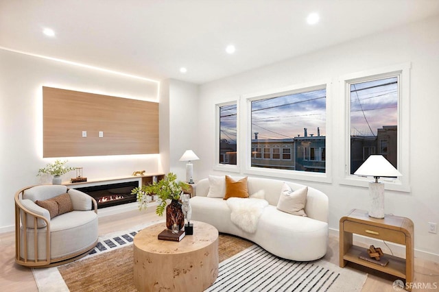 living area with recessed lighting, baseboards, a glass covered fireplace, and wood finished floors