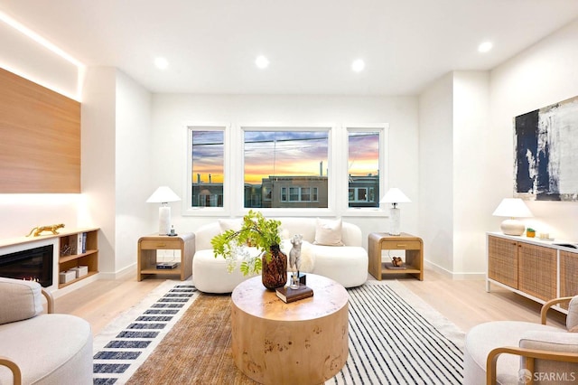 sitting room featuring light wood finished floors, recessed lighting, baseboards, and a glass covered fireplace
