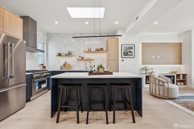 kitchen featuring premium appliances, modern cabinets, tasteful backsplash, wall chimney exhaust hood, and a kitchen bar